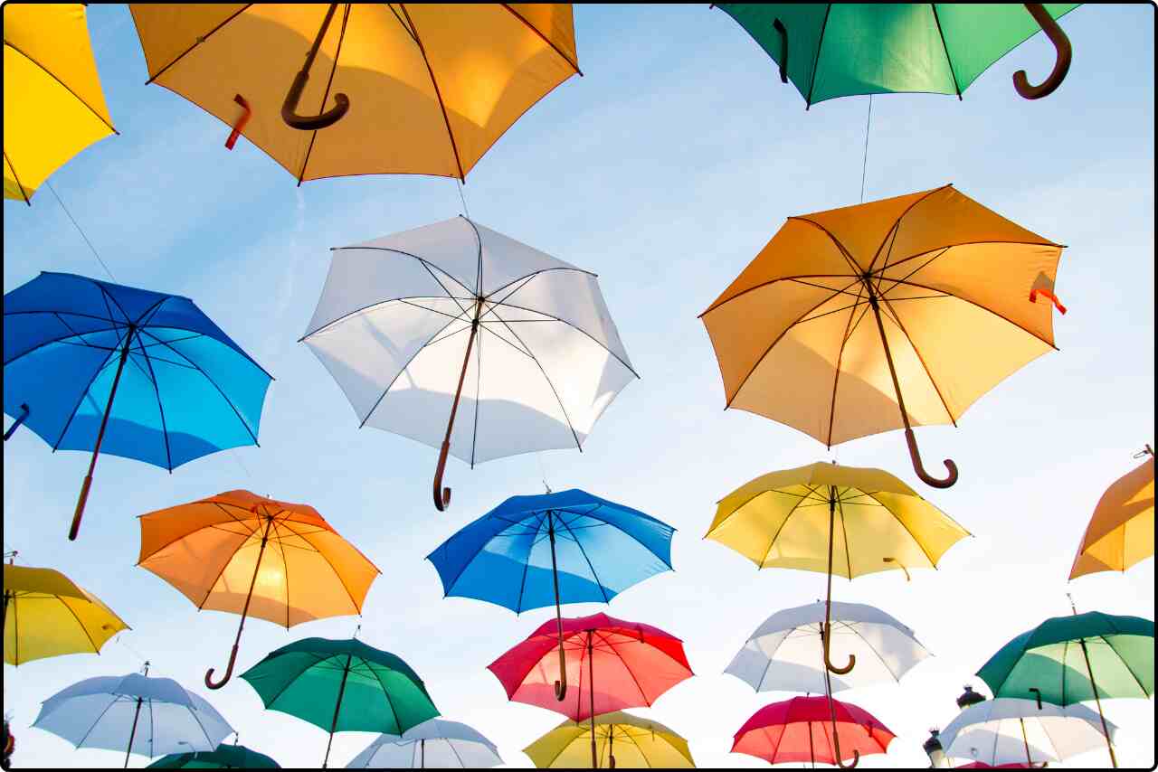 Assorted-color straight umbrellas hanging from a black wire against a clear blue sky.